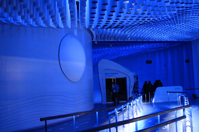 This theater inside the Climate and Environment Pavilion features a ceiling of mirrored stalactite-like cylinders and a wall with a dome-like protrusion. During the presentation, the wall becomes a projection surface, and illustrated images of an earth in peril are projected onto the dome.